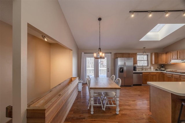 kitchen with appliances with stainless steel finishes, vaulted ceiling with skylight, light hardwood / wood-style floors, and decorative light fixtures