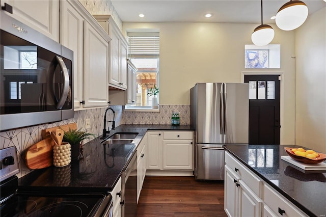 kitchen featuring sink, hanging light fixtures, stainless steel appliances, dark hardwood / wood-style floors, and dark stone counters