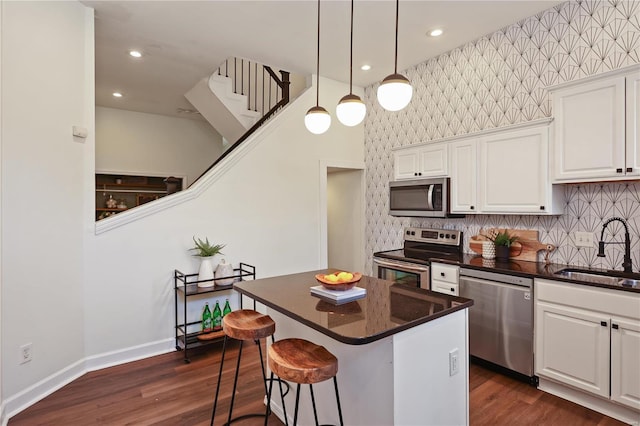 kitchen featuring sink, appliances with stainless steel finishes, white cabinetry, a center island, and decorative light fixtures