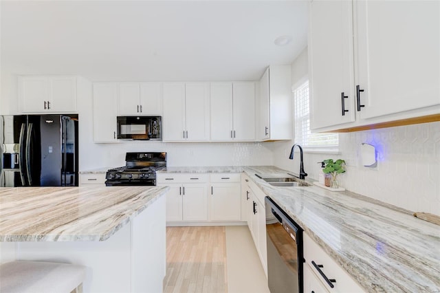 kitchen featuring a breakfast bar, sink, white cabinets, light stone counters, and black appliances