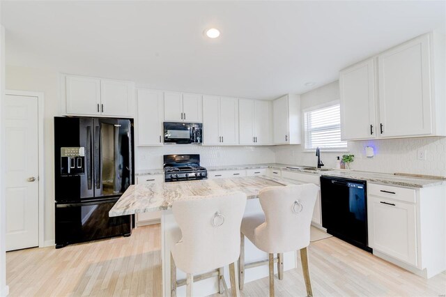 kitchen with light stone counters, black appliances, white cabinets, and a kitchen island