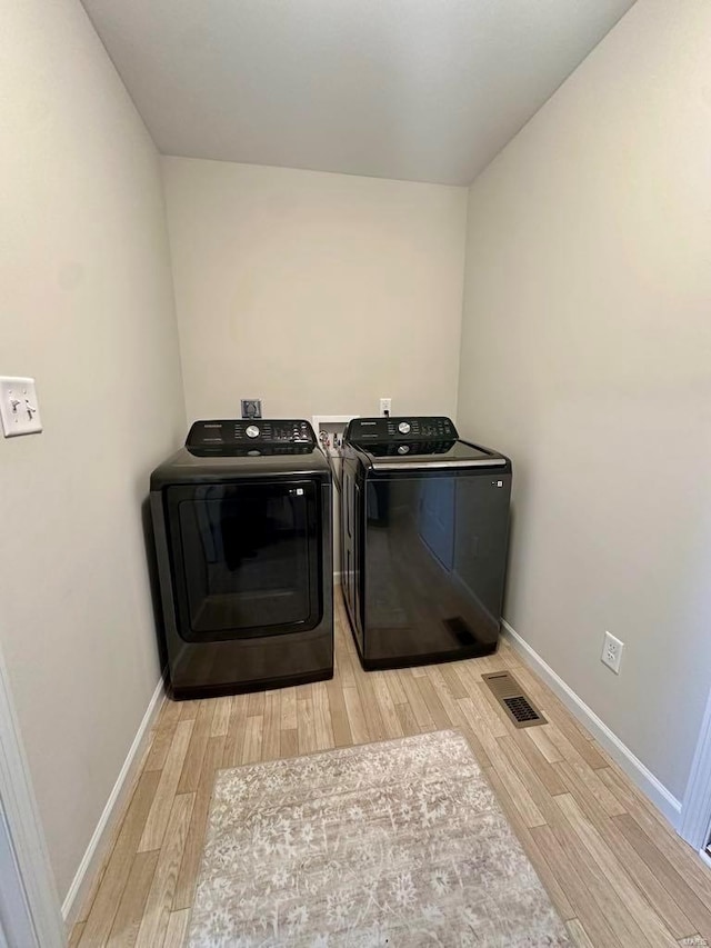 clothes washing area featuring separate washer and dryer and light hardwood / wood-style floors