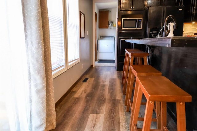 kitchen with washer / dryer, visible vents, dark wood-style floors, stainless steel microwave, and black refrigerator with ice dispenser