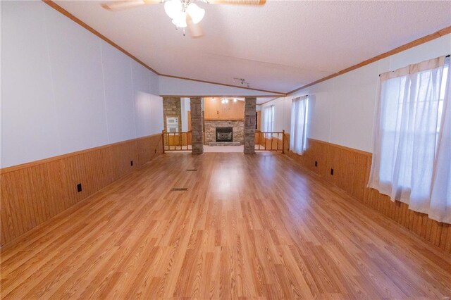 unfurnished living room with crown molding, a stone fireplace, and light wood-type flooring