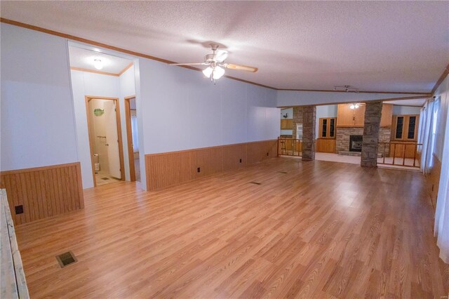 unfurnished living room with crown molding, ceiling fan, a fireplace, a textured ceiling, and light wood-type flooring