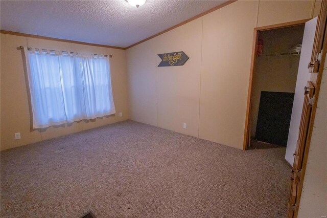 empty room featuring vaulted ceiling, ornamental molding, carpet floors, and a textured ceiling