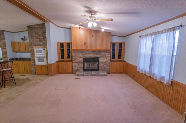 unfurnished living room with a stone fireplace, wood walls, lofted ceiling, ornamental molding, and a textured ceiling