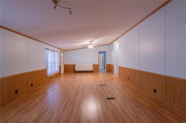 empty room with wood walls, ornamental molding, and light wood-type flooring