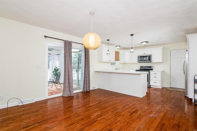 kitchen featuring white cabinetry, decorative light fixtures, appliances with stainless steel finishes, dark hardwood / wood-style flooring, and kitchen peninsula