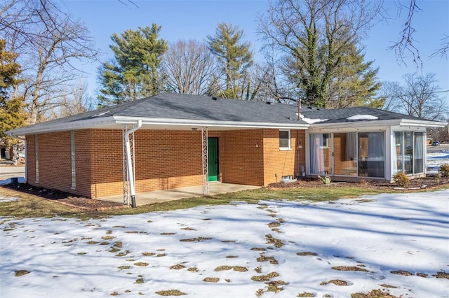 snow covered back of property featuring a sunroom