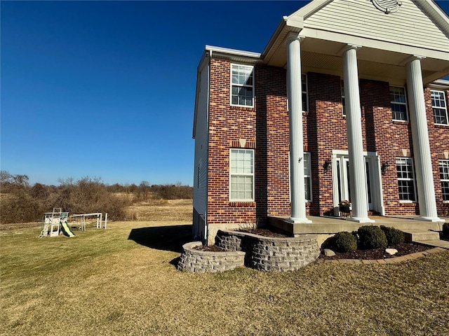 view of side of property featuring a playground, a lawn, and brick siding