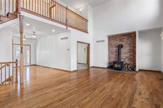 unfurnished living room featuring a towering ceiling, wood-type flooring, and a wood stove