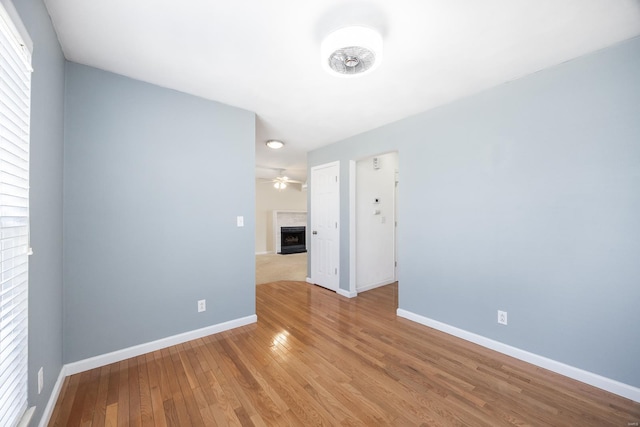 unfurnished room featuring a ceiling fan, wood-type flooring, a fireplace, and baseboards