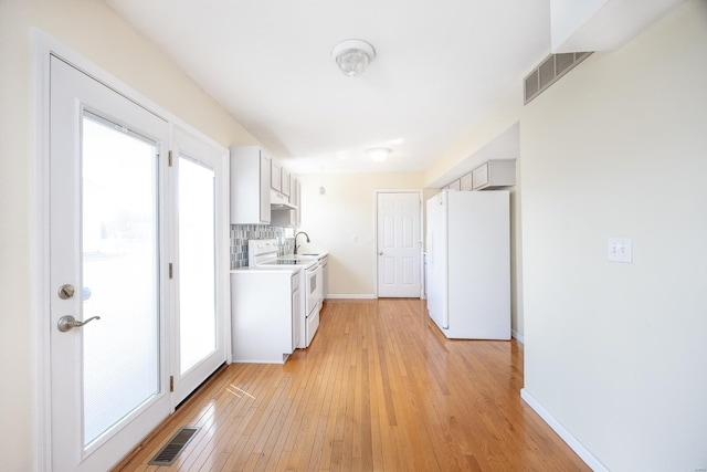 kitchen with white appliances, visible vents, a sink, light countertops, and backsplash