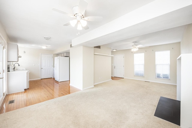 unfurnished living room featuring light carpet, baseboards, visible vents, and a sink