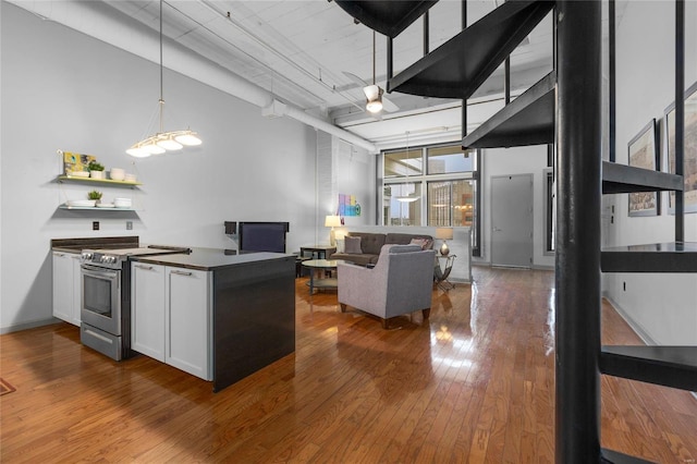 kitchen featuring dark wood-type flooring, white cabinetry, hanging light fixtures, a towering ceiling, and stainless steel range with electric cooktop