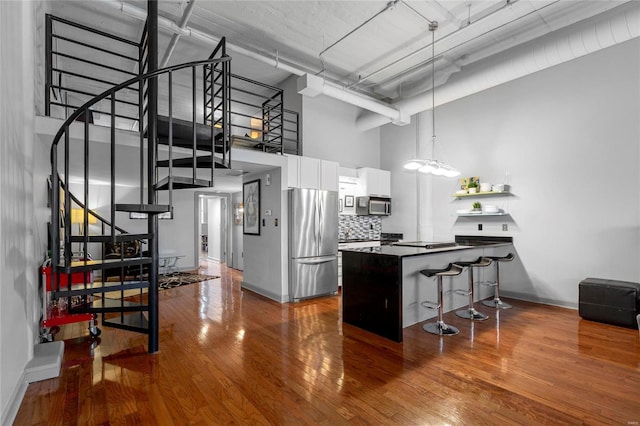 kitchen with appliances with stainless steel finishes, a towering ceiling, decorative light fixtures, white cabinets, and a kitchen breakfast bar