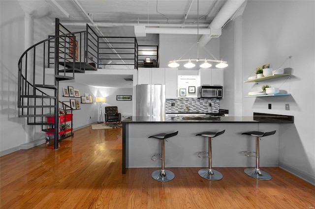 kitchen featuring appliances with stainless steel finishes, a towering ceiling, a kitchen breakfast bar, white cabinets, and kitchen peninsula