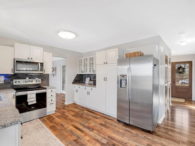 kitchen featuring appliances with stainless steel finishes, tasteful backsplash, white cabinetry, hardwood / wood-style flooring, and light stone countertops