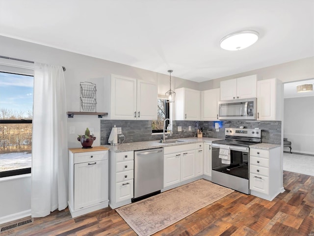 kitchen featuring dark wood-type flooring, sink, white cabinetry, decorative light fixtures, and stainless steel appliances