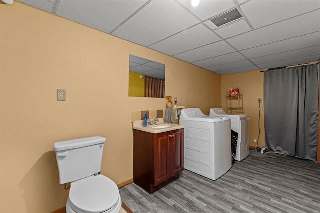 bathroom featuring hardwood / wood-style flooring, washing machine and dryer, vanity, a drop ceiling, and toilet