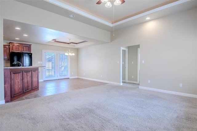 unfurnished living room with a tray ceiling, ceiling fan with notable chandelier, and light carpet