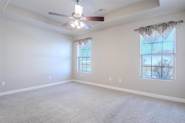 carpeted spare room with a raised ceiling and ceiling fan