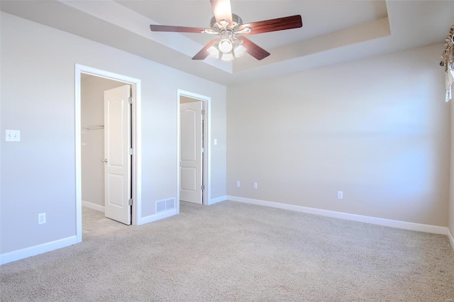 unfurnished bedroom with a spacious closet, light carpet, a tray ceiling, a closet, and ceiling fan