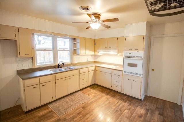 kitchen with light hardwood / wood-style flooring, sink, white oven, and cream cabinetry