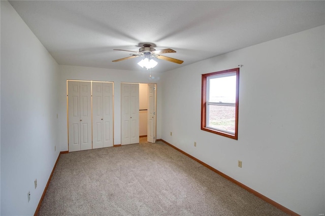 unfurnished bedroom featuring ceiling fan, multiple closets, and carpet