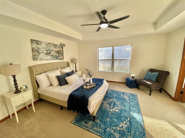 carpeted bedroom with a raised ceiling and ceiling fan