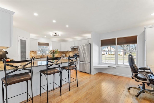 kitchen with white cabinetry, dark stone countertops, a kitchen bar, stainless steel appliances, and light wood-type flooring