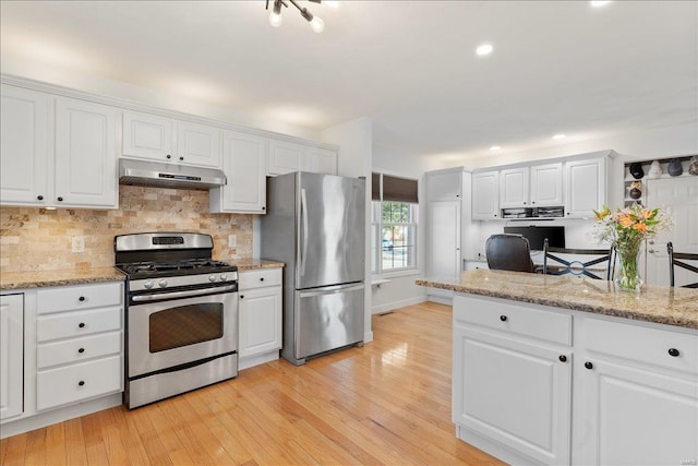 kitchen with tasteful backsplash, light wood-type flooring, stainless steel appliances, light stone countertops, and white cabinets