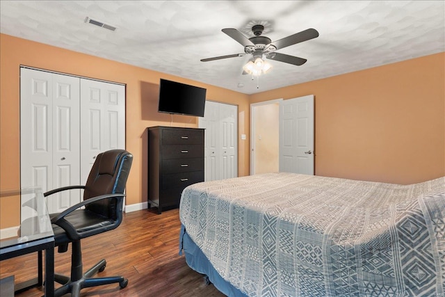 bedroom featuring multiple closets, dark hardwood / wood-style floors, a textured ceiling, and ceiling fan