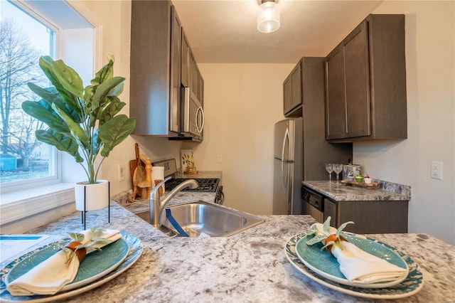 kitchen featuring appliances with stainless steel finishes, light stone countertops, sink, and dark brown cabinets