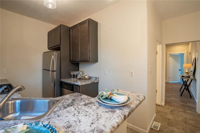 kitchen with light stone counters, dark brown cabinetry, stainless steel appliances, and sink