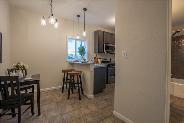 kitchen with appliances with stainless steel finishes, pendant lighting, a kitchen breakfast bar, light stone counters, and kitchen peninsula