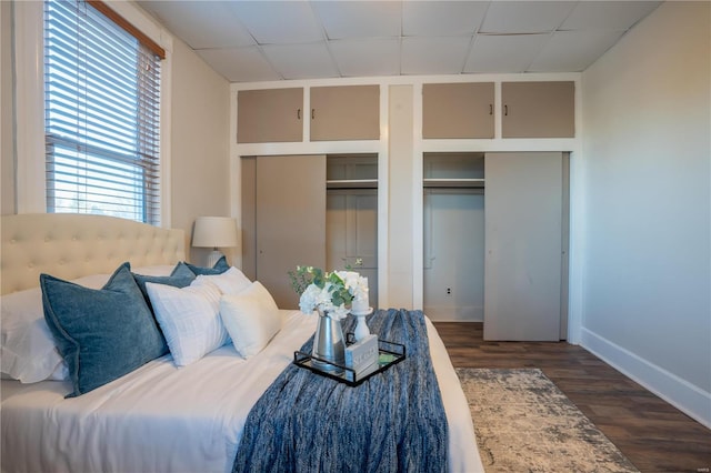 unfurnished bedroom featuring multiple closets, dark wood-type flooring, and a drop ceiling