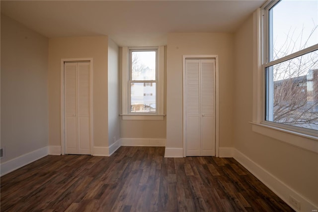 unfurnished bedroom with dark wood-type flooring and multiple closets