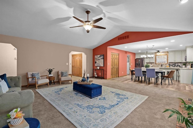 carpeted living room with ceiling fan with notable chandelier and vaulted ceiling