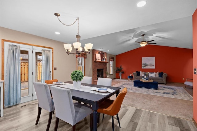 dining room with a brick fireplace, ceiling fan with notable chandelier, lofted ceiling, and light hardwood / wood-style floors