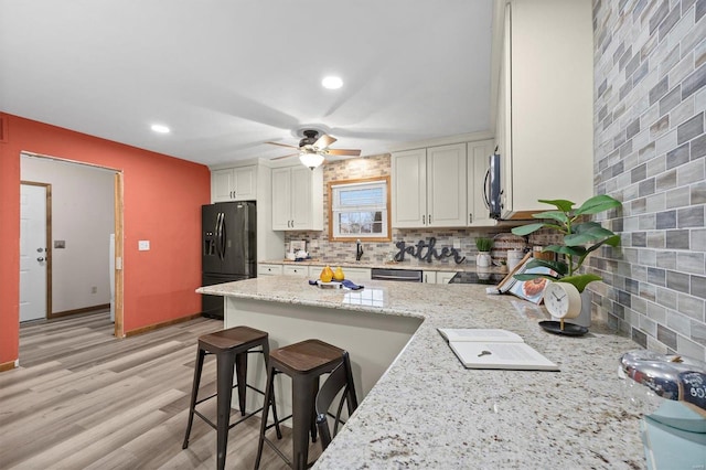 kitchen with a breakfast bar area, tasteful backsplash, black refrigerator with ice dispenser, light hardwood / wood-style flooring, and light stone countertops