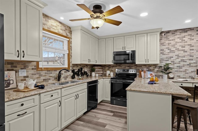 kitchen with sink, black appliances, a breakfast bar, and light stone countertops