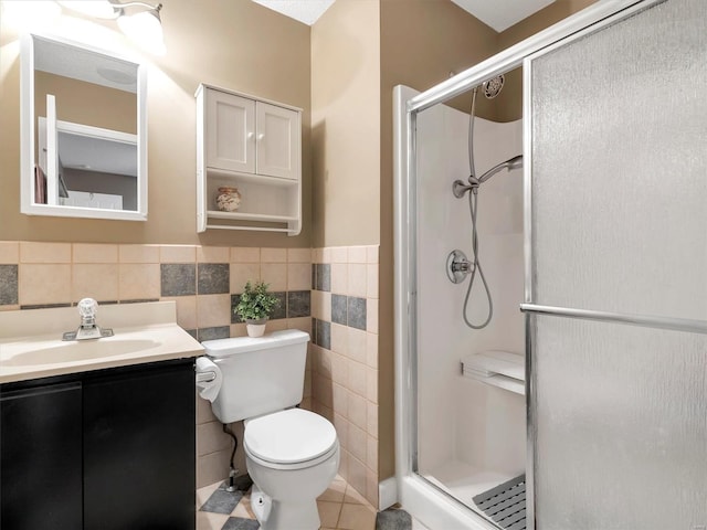 bathroom with a shower with door, vanity, tile walls, and toilet