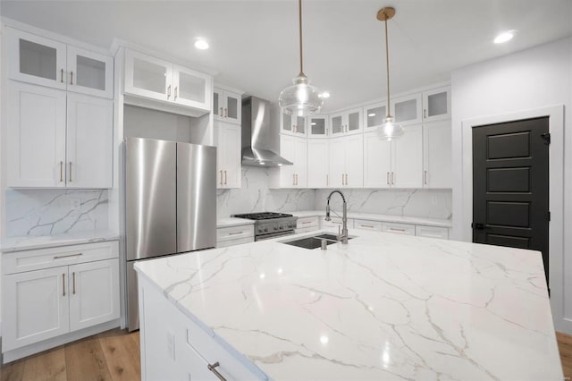 kitchen with wall chimney range hood, sink, appliances with stainless steel finishes, hanging light fixtures, and white cabinets