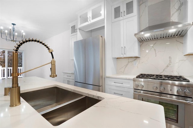 kitchen featuring wall chimney exhaust hood, white cabinetry, light stone counters, stainless steel appliances, and decorative backsplash