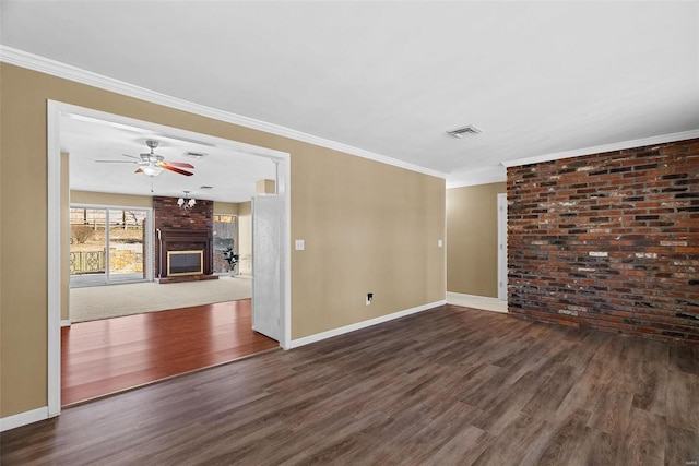 spare room with crown molding, ceiling fan, dark hardwood / wood-style floors, a fireplace, and brick wall