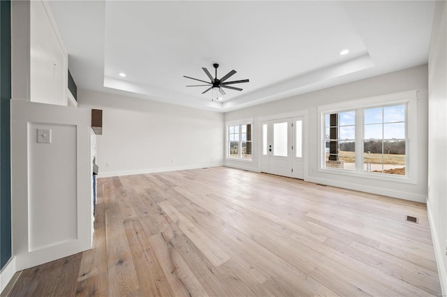 unfurnished living room featuring a raised ceiling, ceiling fan, and light wood-type flooring