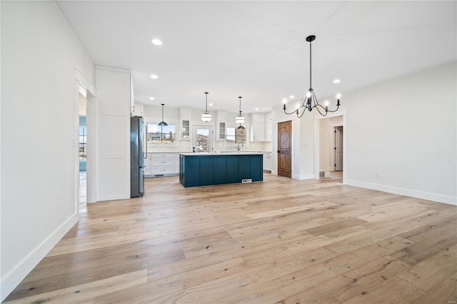 kitchen with stainless steel refrigerator, hanging light fixtures, a notable chandelier, light hardwood / wood-style floors, and white cabinets