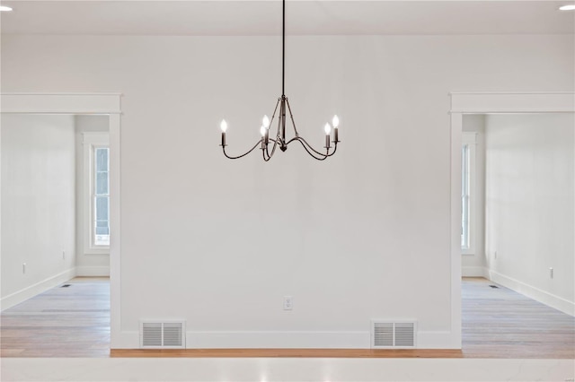 unfurnished dining area featuring a notable chandelier, plenty of natural light, and light wood-type flooring